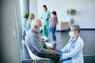 Obraz premium Caring female doctor consoling distraught mature man while holding his hand in waiting room at medical clinic.
