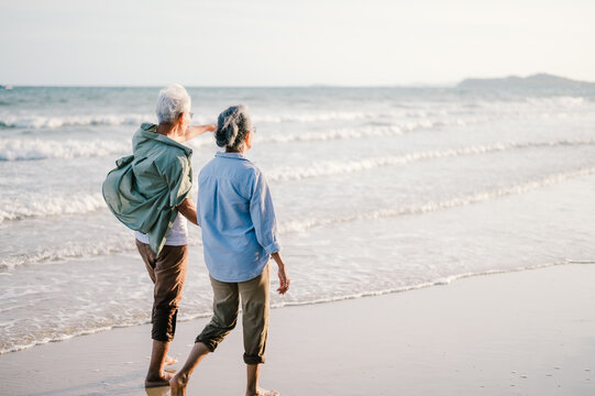 Elderly Asian couple walking on the beach at sunset
