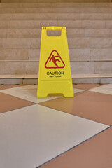 Yellow sign with the words Caution Wet Floor on tiled floor. The concept of cleaning, cleaning service, hotel, security measures. Sign showing warning of caution wet floor