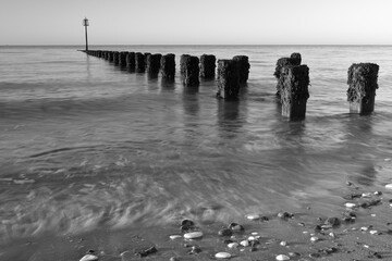Black and white photograph of groynes at the north beach in Bridlington at dawn, with motion blur of the waves.