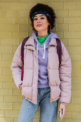 Stylish african american woman standing near yellow brick wall