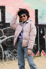 Obraz premium African american woman in sunglasses smiling near blurred graffiti outdoors