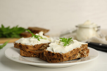 Bread with cream cheese and arugula on white wooden table