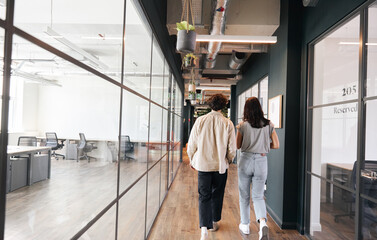 Rear view of young couple walking to office along walkway in open plan building