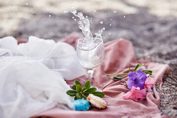Obraz na płótnie Canvas Explosion of cocktail in wine glass on beach with flowers and macaroons. Delicate silk materials and bokeh background. Refreshing summer concept. High quality photo