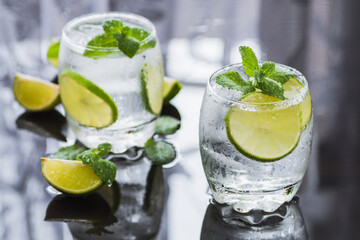 Glasses of cold water with lime slices with mint leaves and ice cubes, a refreshing drink on the shining surface of the table, helpful in a detox diet or in weight loss, hydration concept.