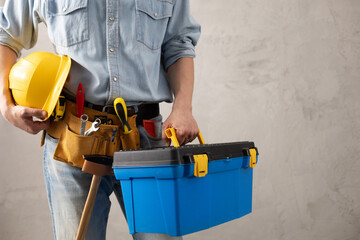 Man worker holding construction helmet and toolbox near wall. Male hand and construction tools - 441193112