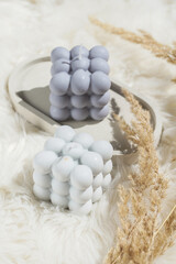 Two grey-blue and white bubble candles on a concrete tray on pastel background, a close up