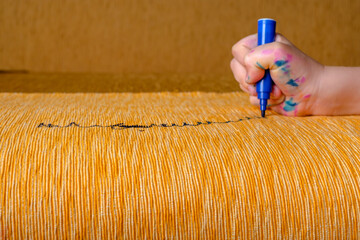 Children's hand draws a blue felt-tip pen on the upholstery of the sofa. 