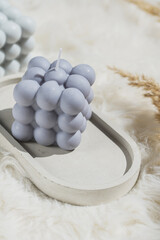 Two grey-blue and white bubble candles on a concrete tray on pastel background, a close up