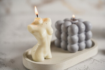 A grey bubble candle and a white candle shaped as a female body on a concrete tray
