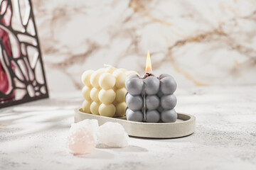 Two grey-blue and white bubble candles on a concrete tray on pastel background, a close up