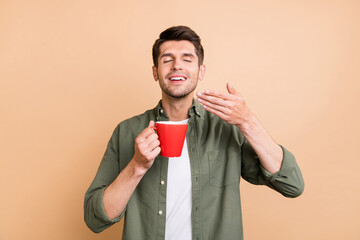 Photo of charming happy cheerful young man smell tea aroma good mood isolated on beige color...