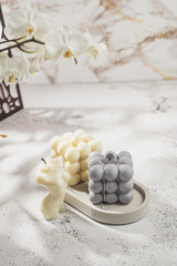 Two grey-blue and white bubble candles on a concrete tray on pastel background, a close up
