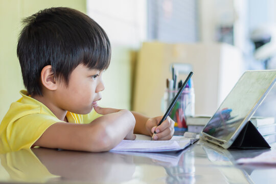 Portrait image of 7-8 years old kid. Happy Asian student child boy using and touching smart pad or tablet for do his homework and online learning. Back to school, Study frome home.