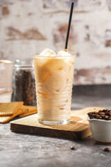 A glass with ice cubes and milk coffee on a wooden board