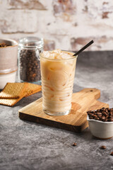 A glass with ice cubes and milk coffee on a wooden board