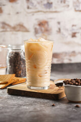 A glass with ice cubes and milk coffee on a wooden board