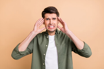 Photo of unhappy tired young guy dressed green shirt arms temples having pain isolated beige color background