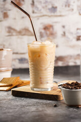 A glass with ice cubes and milk coffee on a wooden board, with brass straw