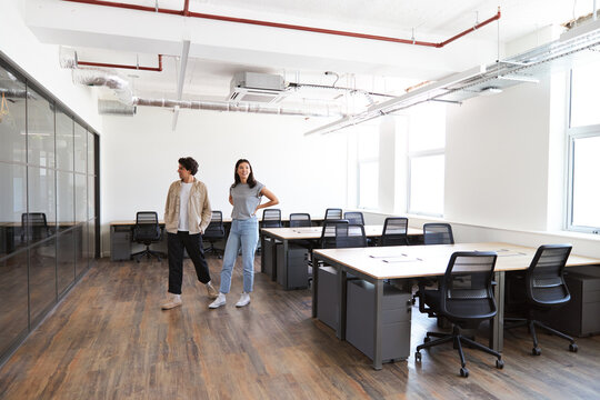 Young couple looking at work space for start up business to rent walking into empty open plan office - Powered by Adobe