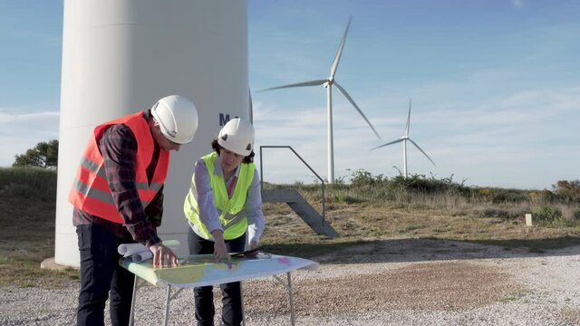 Two workers in a wind farm checking on a map the different wind turbines they have to build.
