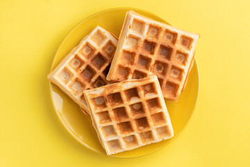 Sweet belgian waffles on yellow plate, isolated on yellow background, Table top view