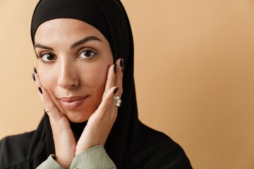 A portrait of the muslim woman wearing black hijab and holding hands near the face and looking at...