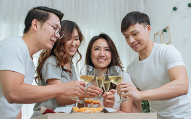 Group four Asian cheerful casual smiley friends making toast or cheers clinking wine glasses together while having party with fun at apartment or home to celebrate farewell or new year or Christmas.