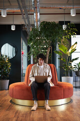 Young man with laptop in seating area of open plan office renting work space for start up business