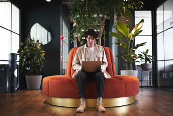 Young man with laptop in seating area of open plan office renting work space for start up business