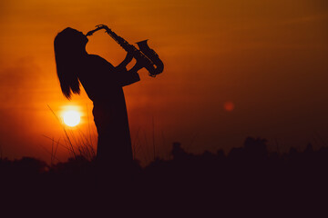 Silhouette of musician with saxophone sunset field,Saxophonist. woman playing on saxophone against...