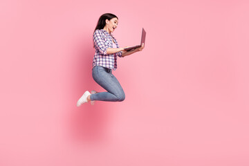 Fototapeta na wymiar Full length body size view of lovely cheerful amazed girl jumping using laptop isolated over pink pastel color background