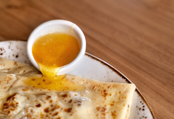 Delicious pancake stuffed with nuts and honey beautifully trickling down on white ceramic plate on wooden table background. Close up. Healthy breakfast concept.