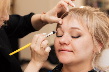 A woman's hand applies and shades the eye shadow with a makeup brush.