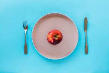 Red apple on a pink plate on blue background. Diet and weight loss concept. Top view, flat lay