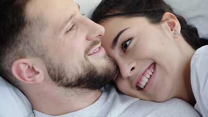 Fototapeta premium joyful brunette woman leaning on bearded boyfriend while resting on bed.