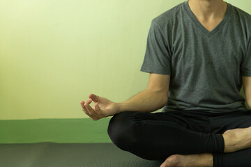 Healthy young Asian man with casual sport clothes meditate on yoga mat when  do yoga at home on home quarantine to reduce stressed, stop the spread of Coronavirus disease or Covid-19.