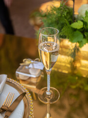 A glass of champagne and a small gift in the form of several macarons in a transparent box, on a luxurious table in a summer luxury restaurant.