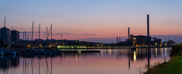 Naklejka premium A beautiful night city skyline against colorful sky. An old power plant casting reflections on the water.