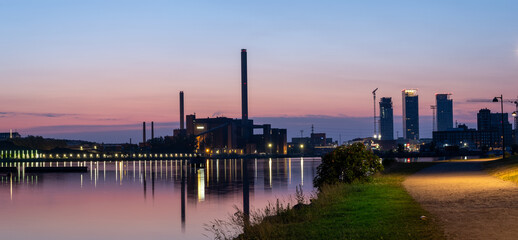A beautiful night city skyline against colorful sky. An old power plant  casting reflections on the water.
