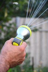 Male hand holding a watering hose on a green background. Watering the garden. Irrigation. Various types of watering