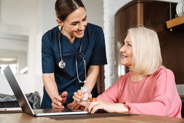 A side view of the smiling woman doctor looking at her elderly patient with a jar of pills in her hands