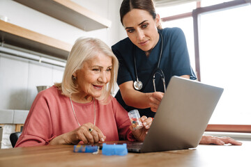 A woman doctor showing her elderly patient with a jar of pills in her hands something in a laptop