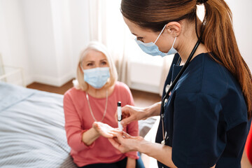 A female doctor measuring blood glucose level with a glucometer to her elderly patient