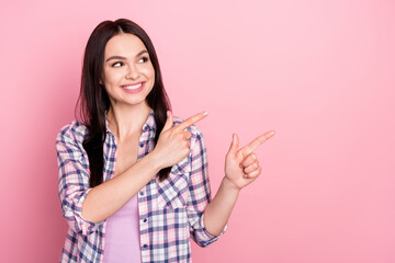 Fototapeta premium Photo of impressed cute young woman wear plaid shirt smiling pointing two fingers looking empty space isolated pink color background