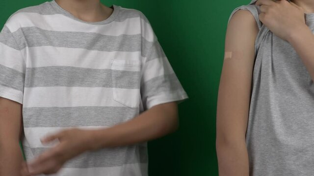 Two boys standing and showing their arm with plaster after vaccination over green screen background. Vaccine and health care for children and teenagers