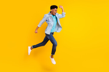 Fototapeta na wymiar Photo of funny hurrying dark skin guy dressed denim shirt running fast jumping high isolated yellow color background