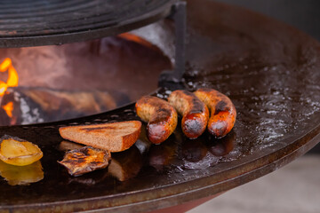 Process of grilling fresh meat sausages, toast bread slice, pepper on round brazier with hot flame...
