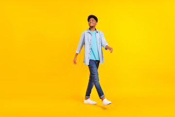 Fototapeta na wymiar Photo of handsome attractive dark skin guy dressed denim shirt walking looking empty space isolated yellow color background